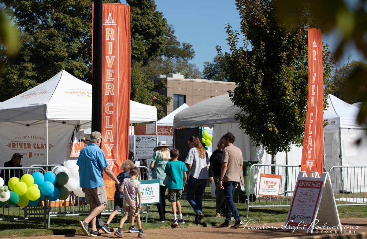 Visitors enter the River Clay 2026 artist market beneath orange festival banners
