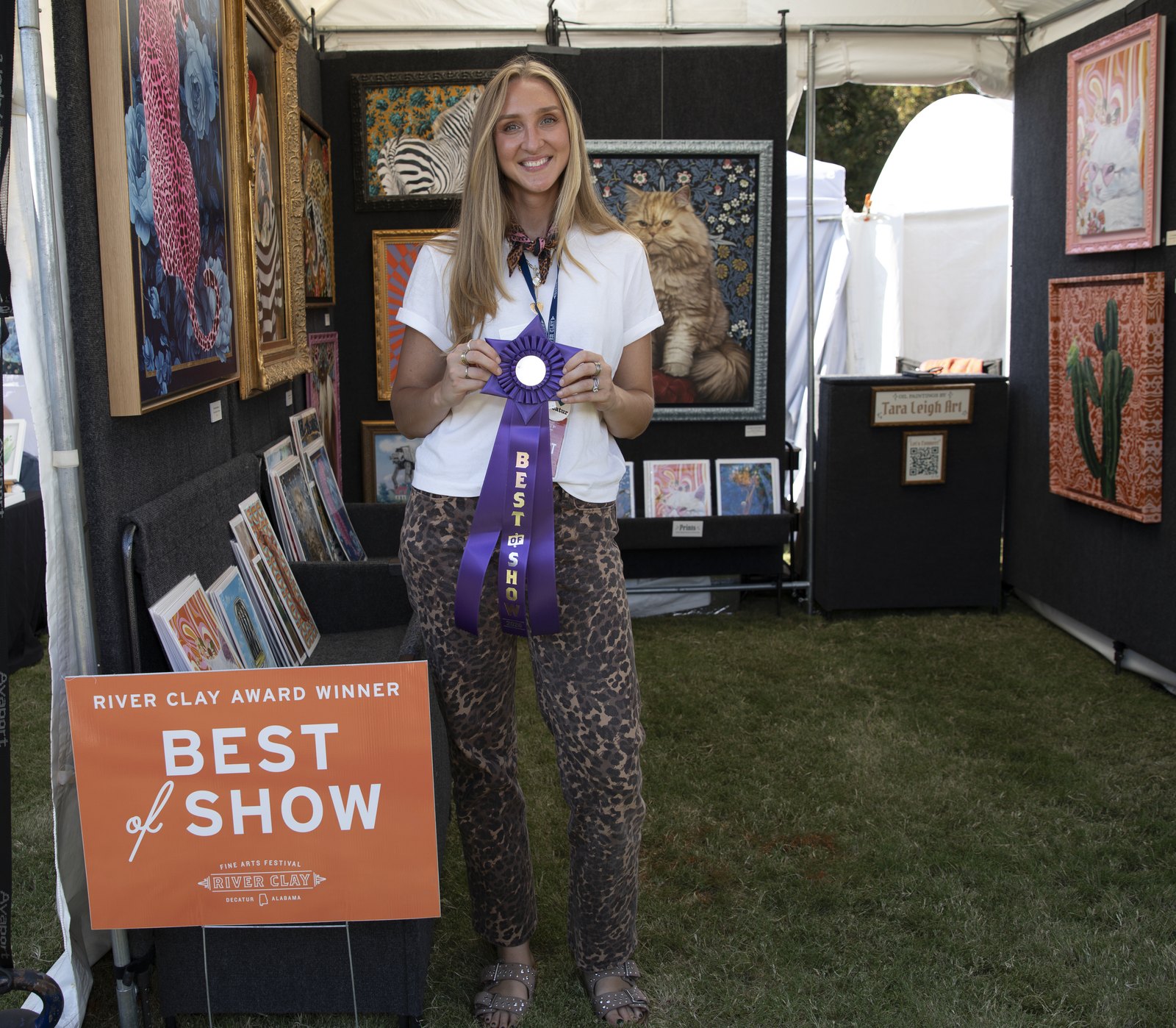 A River Clay artist holds a blue ribbon beside the Best of Show sign